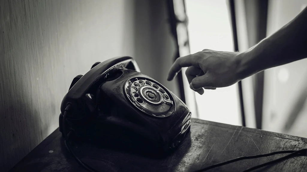 Mão discando um telefone de disco antigo, em preto e branco.