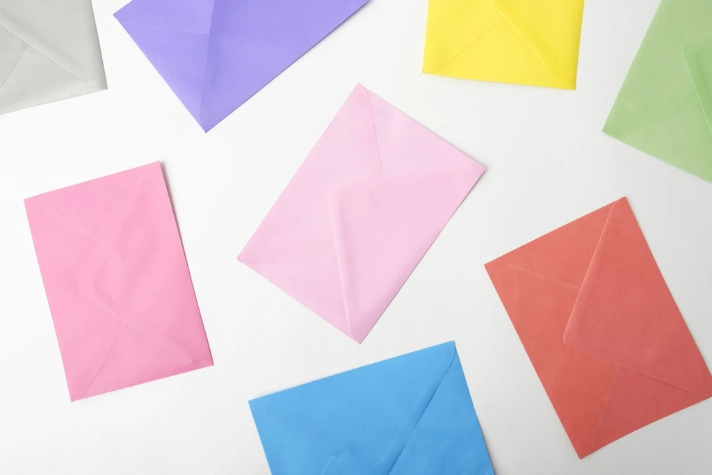 Envelopes de papel em cores pastel espalhados sobre uma superfície branca.